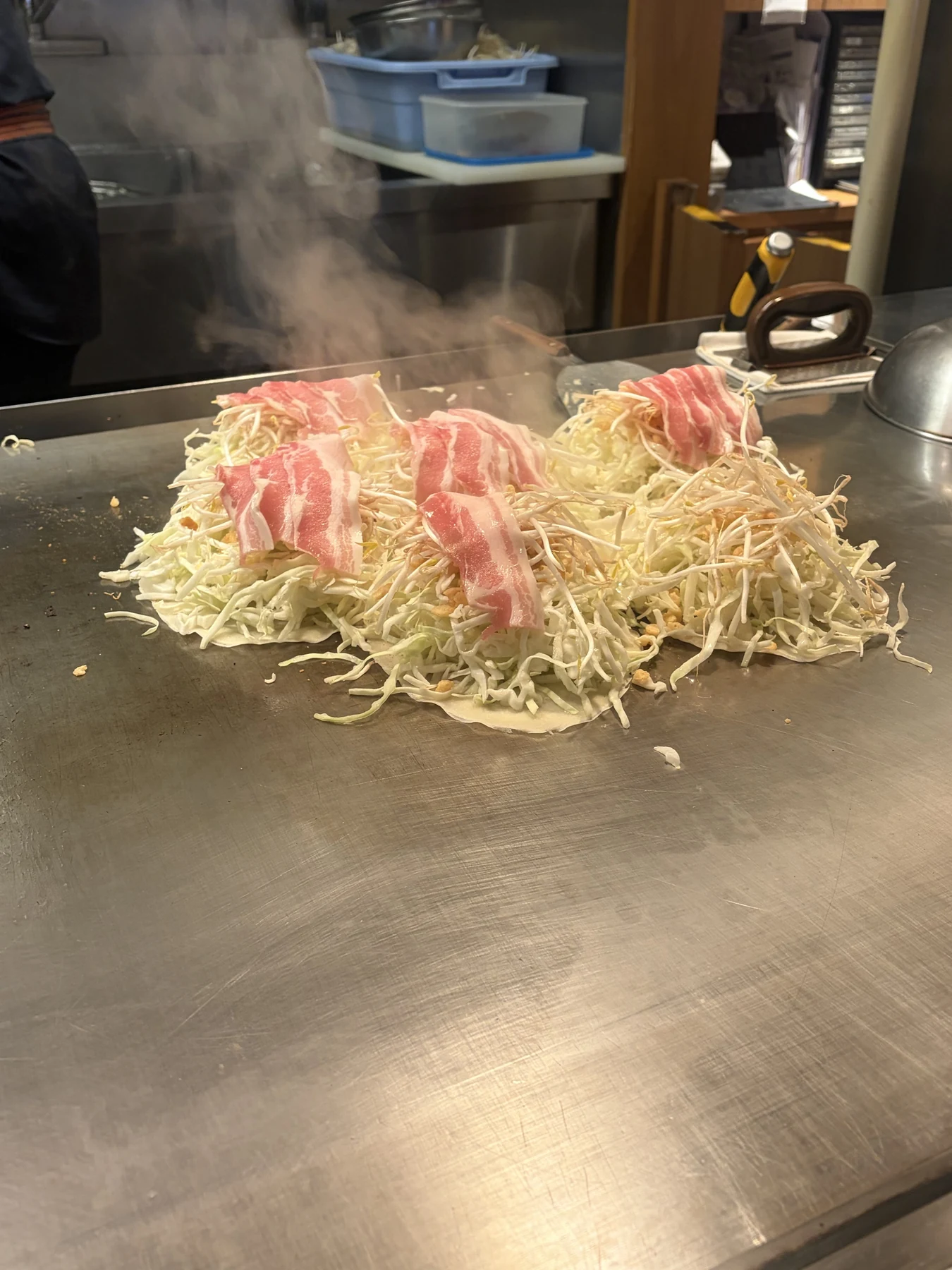 鉄板で焼いているキャベツと豚肉のお好み焼き